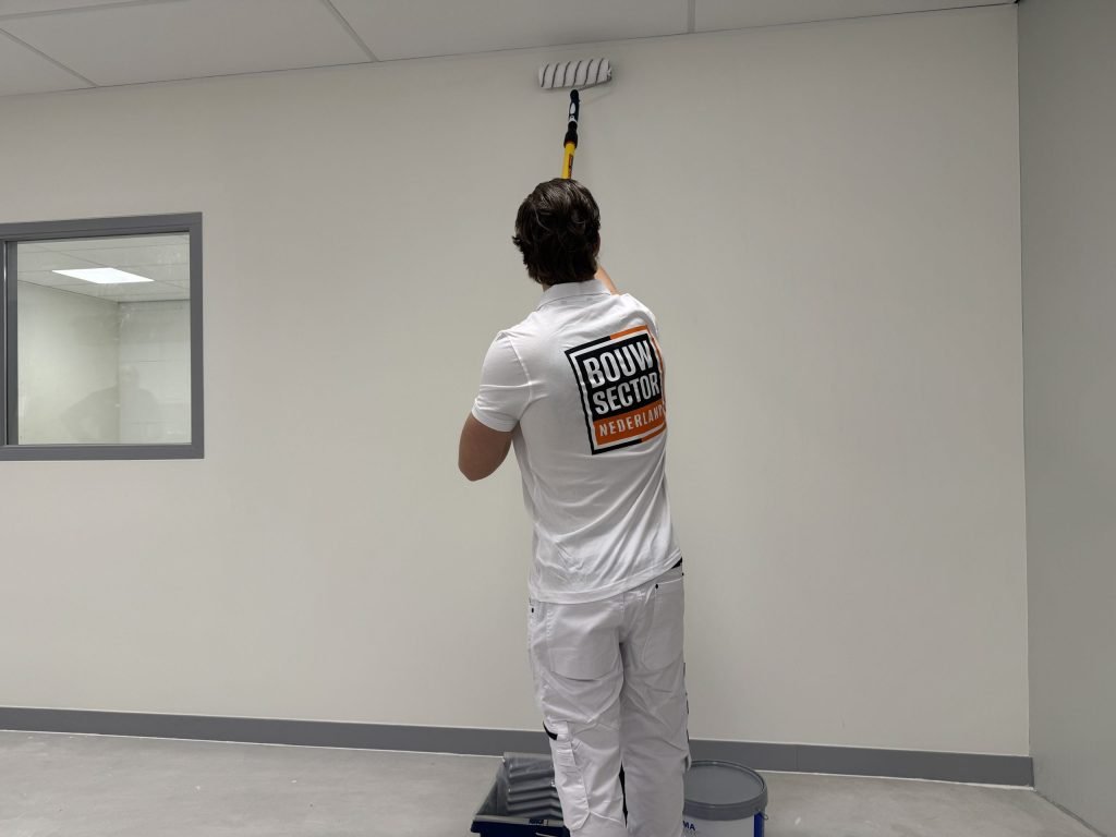Schilder in wit werkshirt saust een lichte muur met een roller aan een verlengsteel