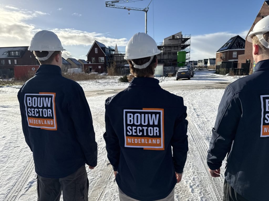 Drie vakmensen van Bouwsector Nederland met witte helm kijken naar nieuwbouw en een bouwkraan